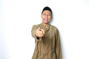 extatisk asiatisk muslim man bär islamic klänning pekande på kamera med skratt isolerat på vit bakgrund foto