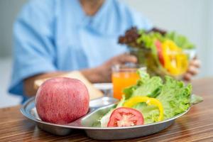 asiatisk senior eller äldre gammal damkvinna som äter frukost vegetabilisk hälsosam mat med hopp och lycklig medan du sitter och är hungrig på sängen på sjukhus. foto