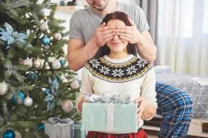ungt par firar jul. en man gav plötsligt en present till sin fru. begreppet familjelycka och välbefinnande foto