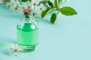 aromatisk eterisk olja i glasflaska och blommor på blå bakgrund. aromaterapi och spa koncept. uppfriskande dofter för avkoppling. foto