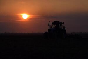 traktor plöjning plog de fält på en bakgrund solnedgång. traktor silhuett på solnedgång bakgrund foto