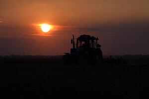 traktor plöjning plog de fält på en bakgrund solnedgång. traktor silhuett på solnedgång bakgrund foto