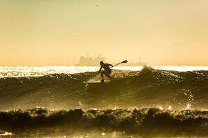 ett oidentifierad surfare rider en stor Vinka med skum på solnedgång foto