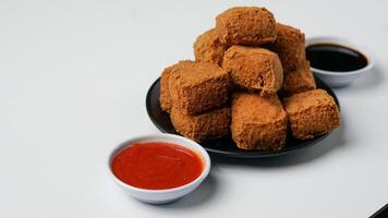 friterad tofu på en svart tallrik med chili sås och ljuv soja sås på en vit bakgrund foto