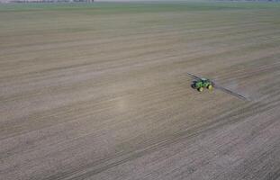 traktor med gångjärn systemet av besprutning bekämpningsmedel. gödsling med en traktor, i de form av ett aerosol, på de fält av vinter- vete. foto