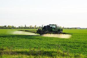 traktor med de hjälp av en spruta sprayer flytande gödselmedel på ung vete i de fält. foto