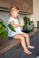 Lycklig bebis flicka Sammanträde på de tabell i de kök och dricka mjölk foto