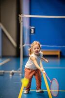 liten flicka tre år gammal spelar badminton i sport ha på sig på inomhus- domstol . hög kvalitet Foto