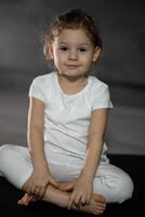 liten söt flicka praktiserande yoga utgör på grå bakgrund i mörk rum foto