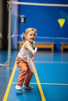 liten flicka tre år gammal spelar badminton i sport ha på sig på inomhus- domstol . hög kvalitet Foto