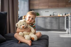 söt liten flicka kramas teddy Björn medan Sammanträde på soffa på Hem foto