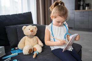 liten flicka spelar läkare med leksaker och teddy Björn på de soffa i levande rum på Hem foto