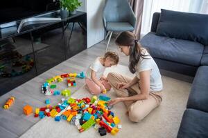 liten flicka spela med konstruktör leksak på golv i Hem med mamma eller kvinna barnvakt, pedagogisk spel, familj på Hem spendera fritid aktiviteter tid tillsammans begrepp foto