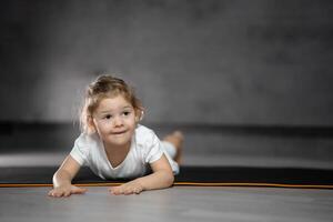 liten söt flicka praktiserande yoga utgör på grå bakgrund i mörk rum. hög kvalitet Foto