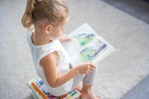 liten flicka är Sammanträde på stack av barns böcker och blad genom en bok med bilder av fe- berättelser foto