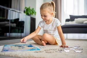 liten blond flicka sitter på Hem på de matta och samlar pussel foto