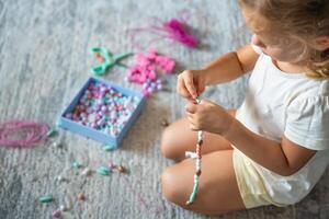 liten flicka framställning trä- pärlor armband på Hem levande rum. barns kreativitet och de utveckling av bra motor Kompetens foto