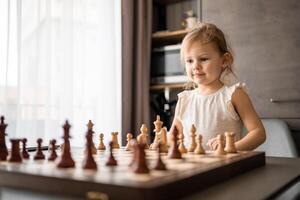liten flicka spelar schack på de tabell i Hem kök. de begrepp tidigt barndom utveckling och utbildning. familj fritid, kommunikation och rekreation. foto