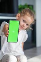 liten flicka är Sammanträde och innehav en smartphone med en Chromakey foto