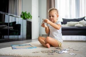 liten blond flicka sitter på Hem på de matta och samlar pussel foto