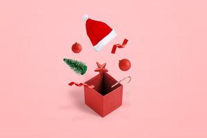 öppnad presentförpackning med dekorationer och hatt kommer ut ur lådan koncept. isometrisk position. pastell rosa bakgrund foto