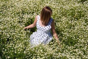 en kvinna i en vit klänning med polka prickar är på en glänta med prästkragar. blomning daisy foto