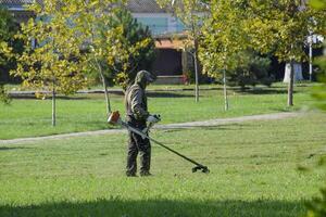 arbetstagare klippning gräs med en bensin borsta. trimmer. foto