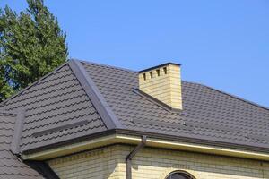 brun korrugerad metall profil tak. skorsten och ventilation av gul tegel. foto