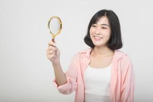 ung asiatisk kvinna innehav förstorande glas över vit bakgrund, analys och finansiera begrepp foto