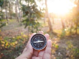 stänga upp av kompass i kvinna hand med skog i de solnedgång tid som bakgrund. de begrepp av värld turism dag, sökande de rätt vägbeskrivning och resa foto