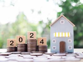 miniatyr- hus, trä- block med siffra 2024 på stack av mynt. de begrepp av betalning beskatta för hus, fast egendom investering, hus inteckning, verklig egendom i ny år 2024. foto