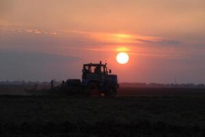 traktor plöjning plog de fält på en bakgrund solnedgång. traktor silhuett på solnedgång bakgrund foto