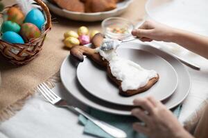 childs händer dekorera påsk kanin formad kaka med glasyr på festlig dekorerad tabell foto
