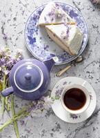 fortfarande liv med svart te och ost kaka, vår bukett, delikat lila blommor foto