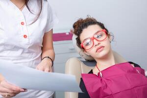 närbild av kvinna patient som visar henne skön vit tänder medan har behandling på dental klinik, tandläkare händer i sudd handskar innehav dental verktyg foto