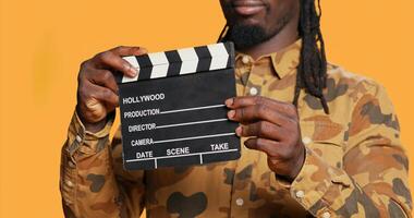 afrikansk amerikan filma producent använder sig av clapperboard för film industri, identifiera Allt tar på filmning produktion. leende direktör innehav flik styrelse till skära scener, skrikande verkan på uppsättning. foto