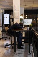 utmattad chef med burnout syndrom vilar på arbete, efter arbetssätt över tid på företag investering Rapportera. trött afrikansk amerikan entreprenör sovande på skrivbord i börja kontor foto