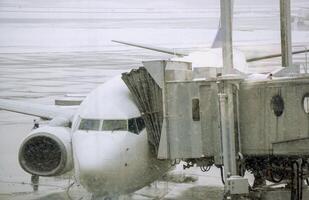 närbild jet bro och vit flygplan parkerad på flygplats jord och bomull snöar i vinter- väder. foto