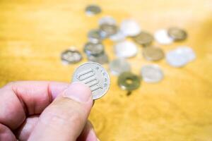 hand plockning upp 100 yen japansk mynt från suddigt mynt högen på trä- tabell bakgrund. foto