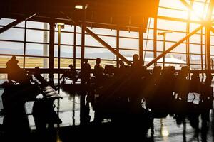 silhuett av människor och turist väntar gå till de plan i en flygplats terminal med luft plan och Sol blossa bakgrund. foto