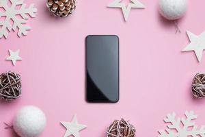 telefon på rosa skrivbord omgiven av juldekorationer. begreppet julshopping och presentförpackning. tom smart telefon för mockup