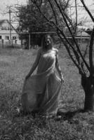 svart och vit Foto, flicka i de trädgård på en äng i en klänning. foto