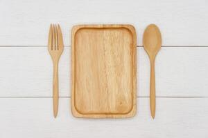 tömma rektangel trä- tallrik med sked och gaffel på vit trä- tabell. topp se bild. foto