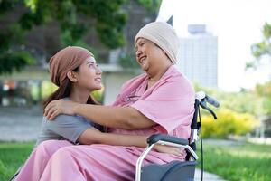 asiatisk försiktig vårdgivare eller sjuksköterska och kvinna med cancer är Sammanträde i en rullstol. i de trädgård. begrepp av Lycklig pensionering med vård från en vårdgivare och besparingar och senior hälsa försäkring. foto