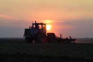 traktor plöjning plog de fält på en bakgrund solnedgång. traktor silhuett på solnedgång bakgrund foto