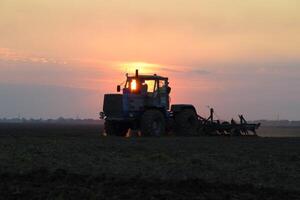 traktor plöjning plog de fält på en bakgrund solnedgång. traktor silhuett på solnedgång bakgrund foto