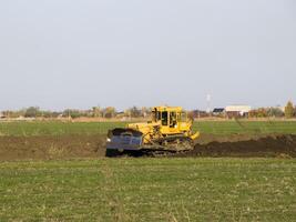 de gul traktor med bifogad grederom gör jord utjämning. foto