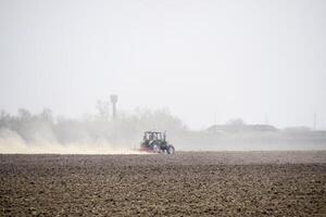 de traktor harvar de jord på de fält och skapar en moln av damm Bakom den foto