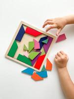 childs hand samlar flerfärgad trä- mosaik- på vit bakgrund. barn löser färgrik tangram foto