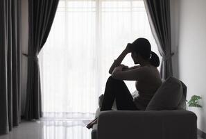 silhuett av en person lidande från depression i de hus, deprimerad kvinna Sammanträde ensam på de soffa känna påfrestning, ledsen och orolig i de mörk rum. person är stressad. foto
